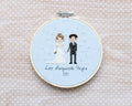 A cross-stitched bride and groom with subtle bubbles hand-stitched around them. It's framed in a wooden embroidery hoop and reads 